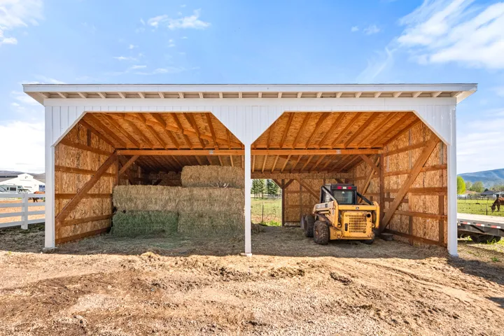 Open-air barn structure featuring white siding and exposed wood framing