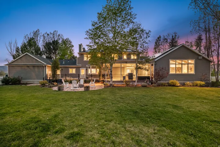 Expansive green lawn with a large, grey-sided residence featuring multiple windows and a covered patio