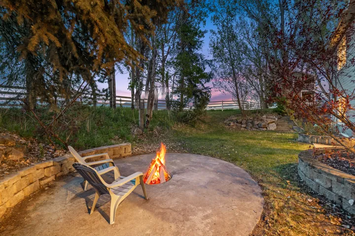 Circular concrete patio featuring a built-in fire pit, surrounded by a stone retaining wall and grassy areas