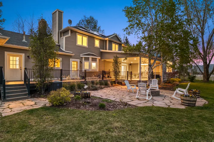 Expansive flagstone patio with a built-in fire pit, surrounded by mature trees and a manicured lawn