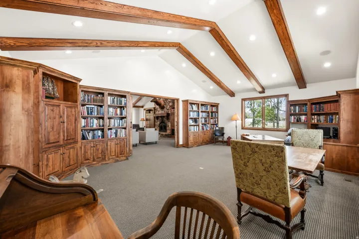 Spacious room featuring vaulted ceilings with exposed wood beams, recessed lighting, expansive built-in wood cabinetry, and wood-framed windows
