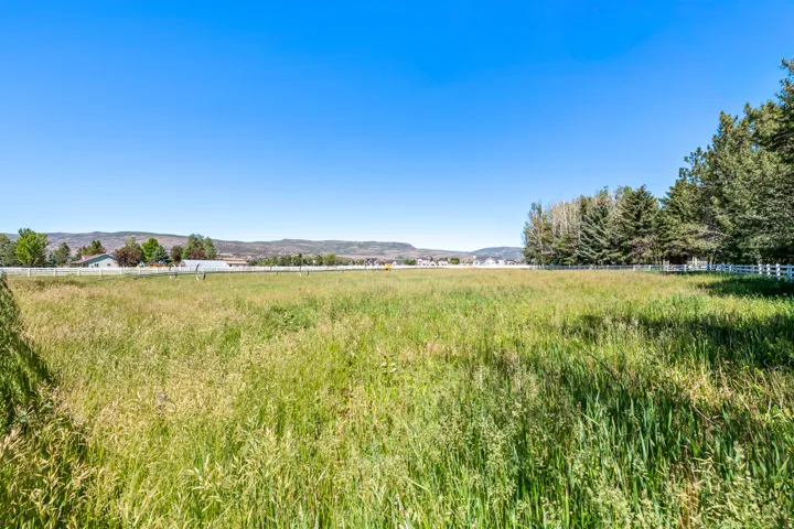 Expansive open pastureland featuring a white post-and-rail fence, mature trees, and distant mountain backdrops