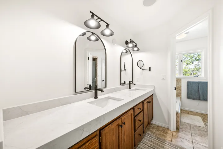 Double vanity featuring a white countertop with integrated sinks, black fixtures, and arched mirrors