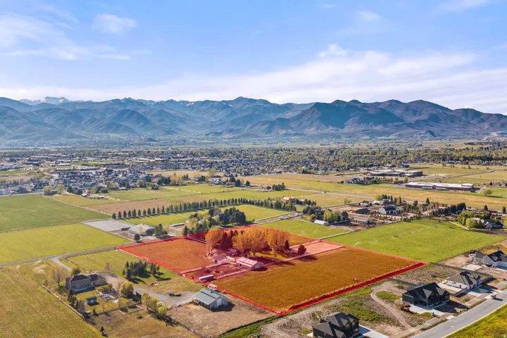 Expansive rural property featuring multiple structures, open fields, mature trees, and mountainous scenery