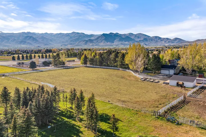 Expansive property featuring a large open field, white perimeter fencing, mature trees, and a stable building