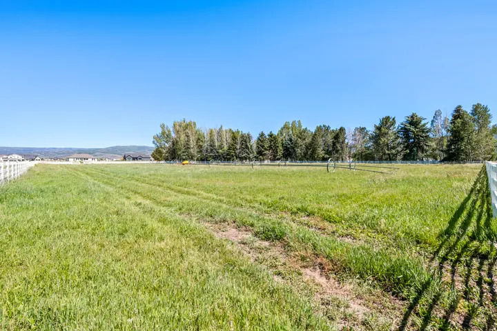Expansive green space featuring perimeter fencing, distant mountain backdrop, and mature trees