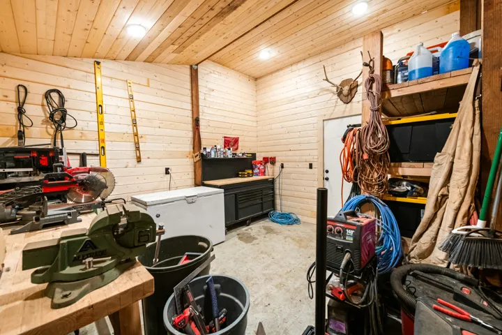 Spacious workshop featuring plank wood walls and ceiling, ample overhead lighting, built-in shelving, and a durable concrete floor