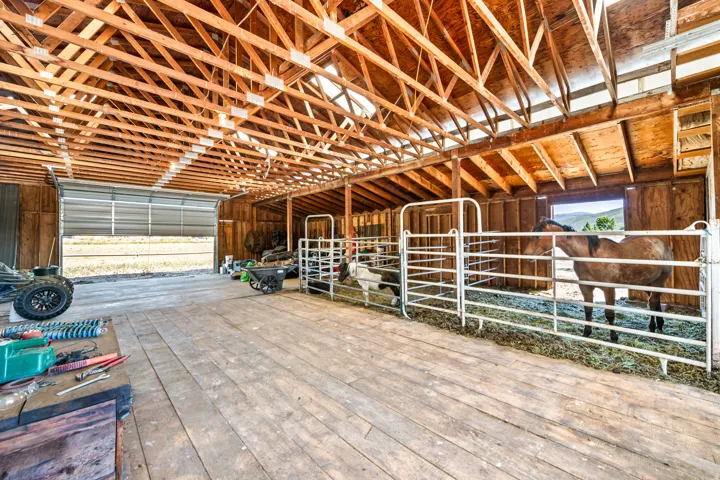 Spacious barn interior featuring exposed wooden rafters, wide plank wood flooring, and extensive natural light