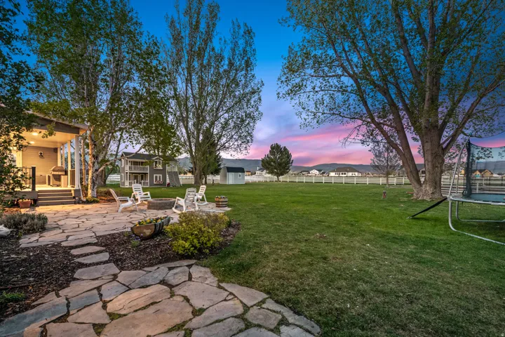 Expansive stone patio with built-in fire pit, surrounded by a large grassy yard