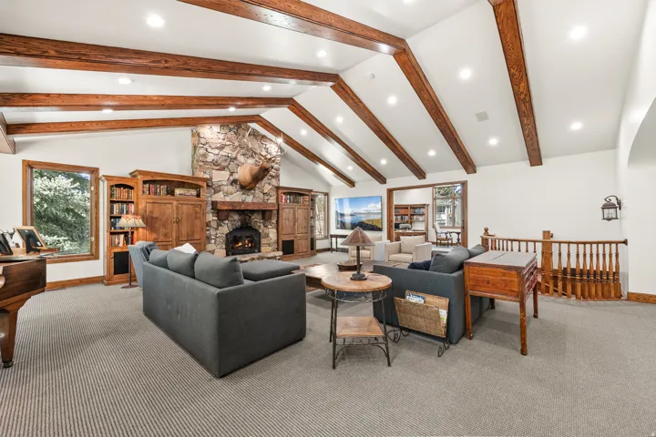 Spacious living area featuring vaulted ceilings with exposed wood beams, a stone fireplace with a wood mantle, recessed lighting, and built-in wood cabinetry