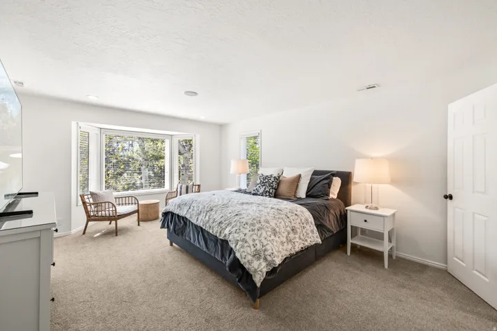 Bright interior space featuring a large bay window with louvered blinds, plush carpeting, recessed lighting, and a paneled interior door