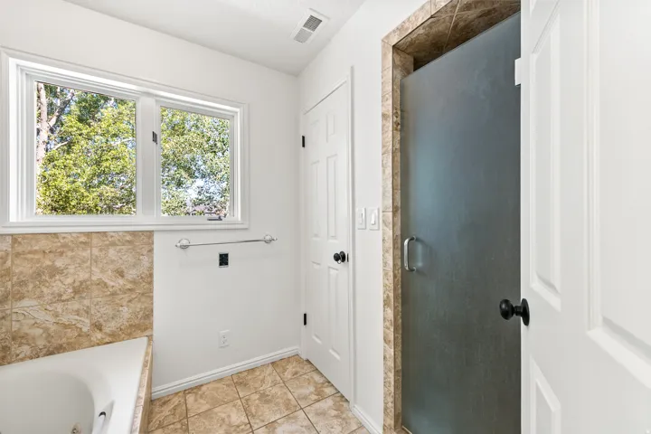 Bathroom featuring a jetted tub with tile surround, a frosted glass shower enclosure with tile accent, tile flooring, and a double window