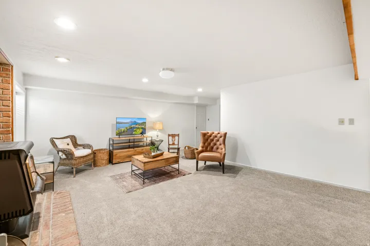 Spacious room featuring light gray carpeting, recessed ceiling lighting, and a brick accent wall with a hearth