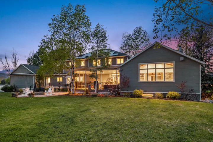 Expansive rear exterior featuring a two-story residence with a covered patio, a separate gabled structure with a large window, and a stone fire pit area