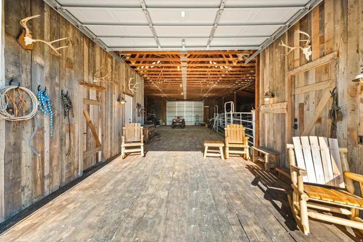 Spacious interior barn with wood-plank walls and flooring, exposed wood beam ceiling, and overhead garage door