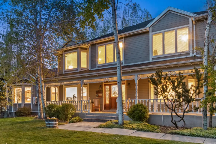 Two-story residential exterior featuring a full-width covered front porch with decorative millwork and white railings, bay windows, and a wood-finish double entry door