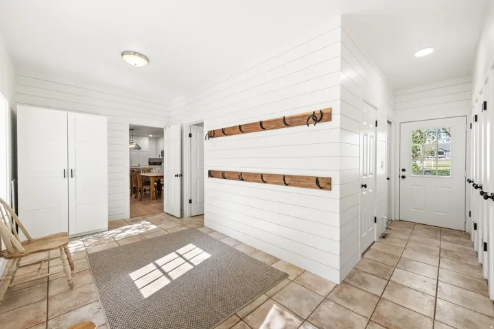 Entryway featuring shiplap walls, ceramic tile flooring, a white paneled door with glass inserts, and built-in wooden coat racks