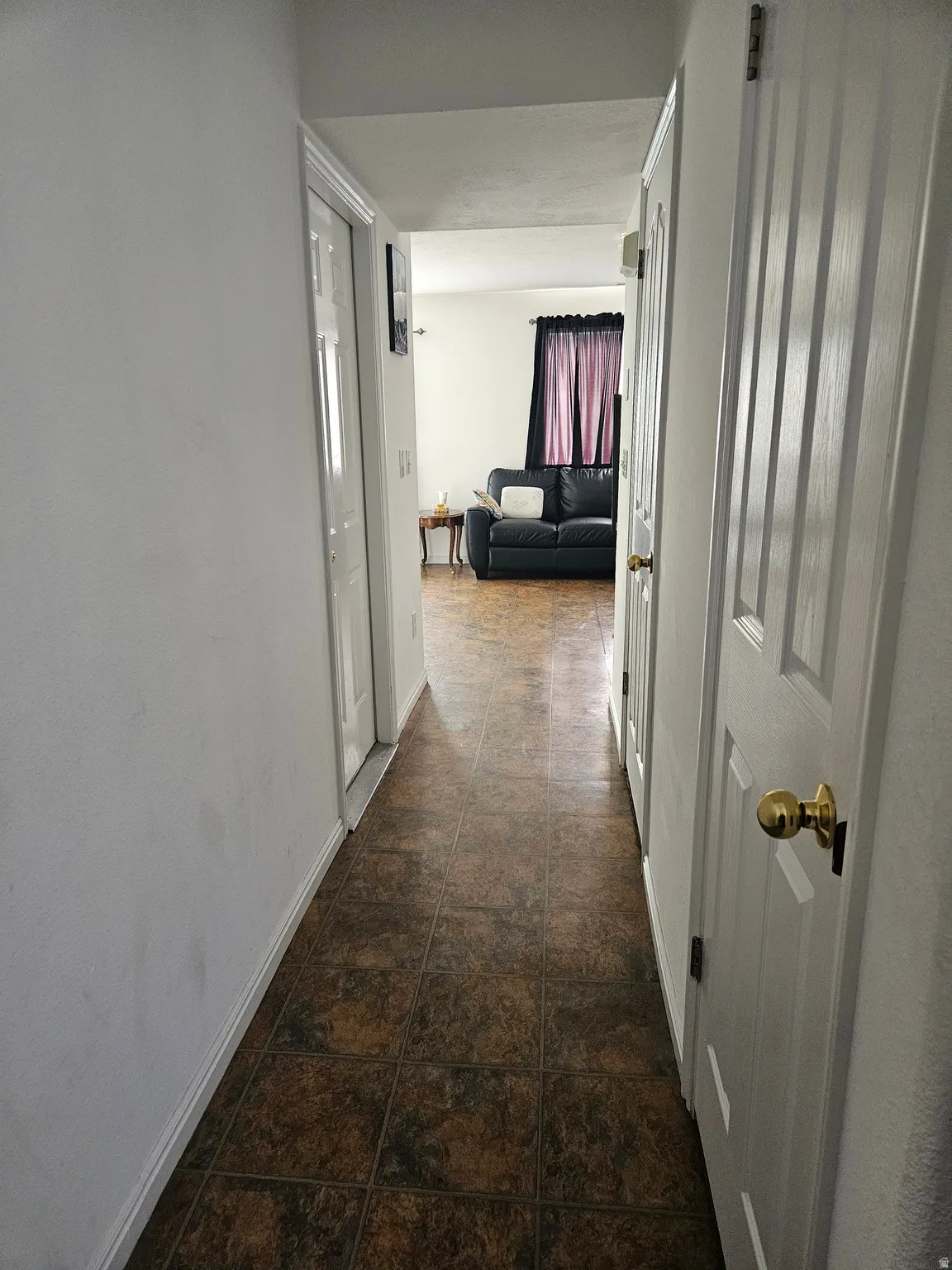 Hallway featuring brown tile flooring, white walls, and white paneled doors with brass hardware