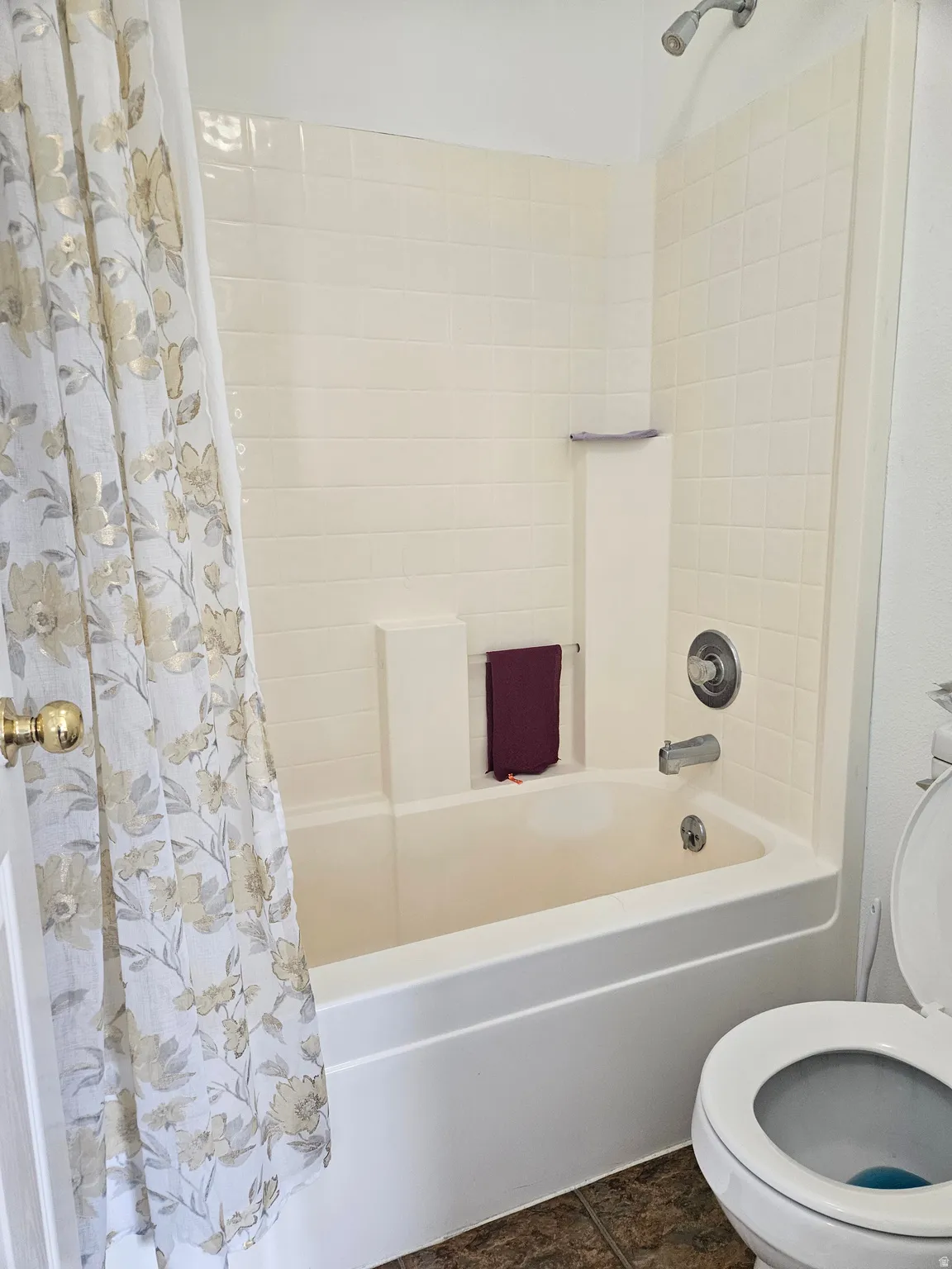 White bathtub with integrated shower, chrome fixtures, and a light-toned tiled surround