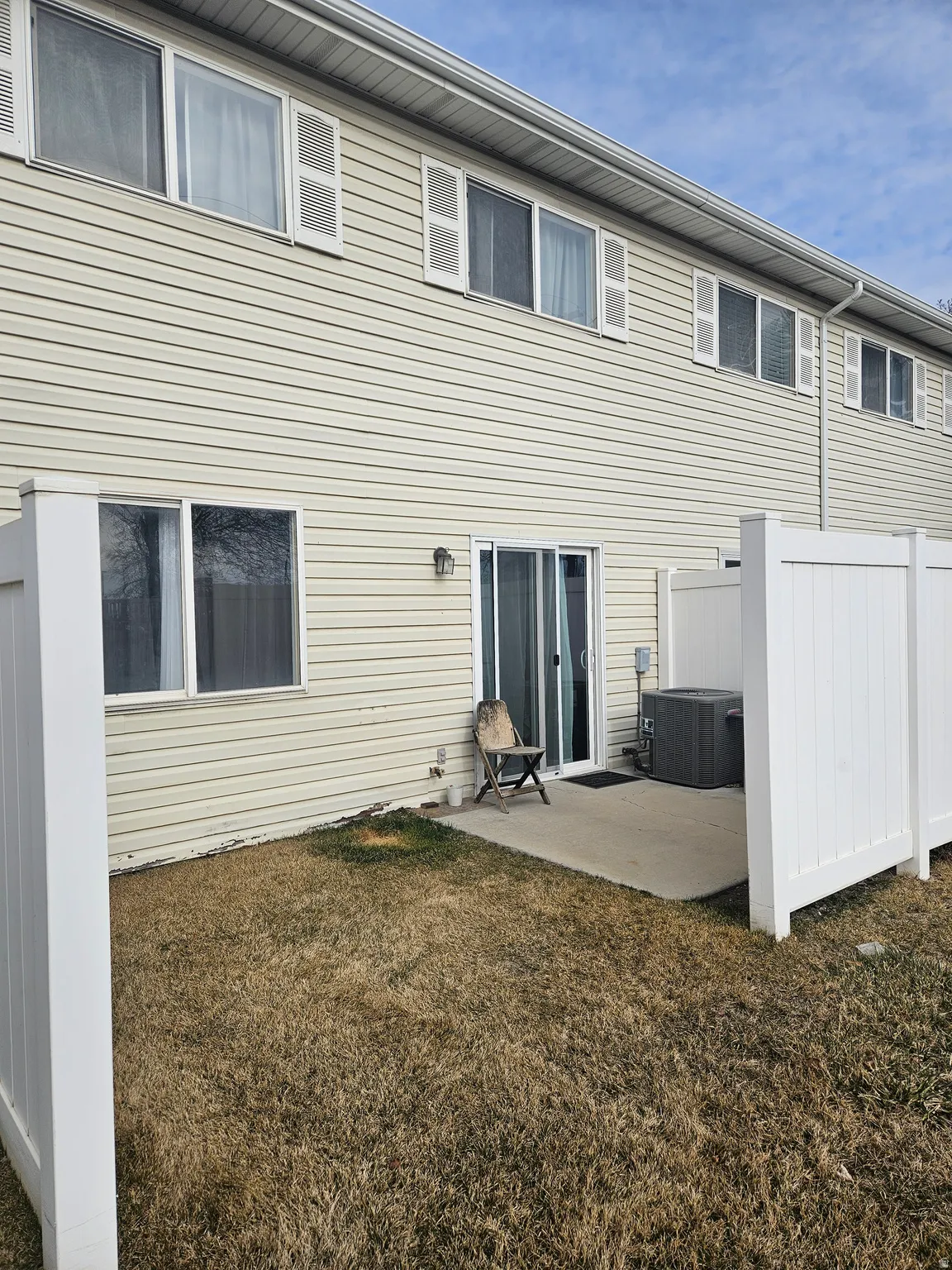 Rear exterior with light-colored siding, a concrete patio, and a privacy fence