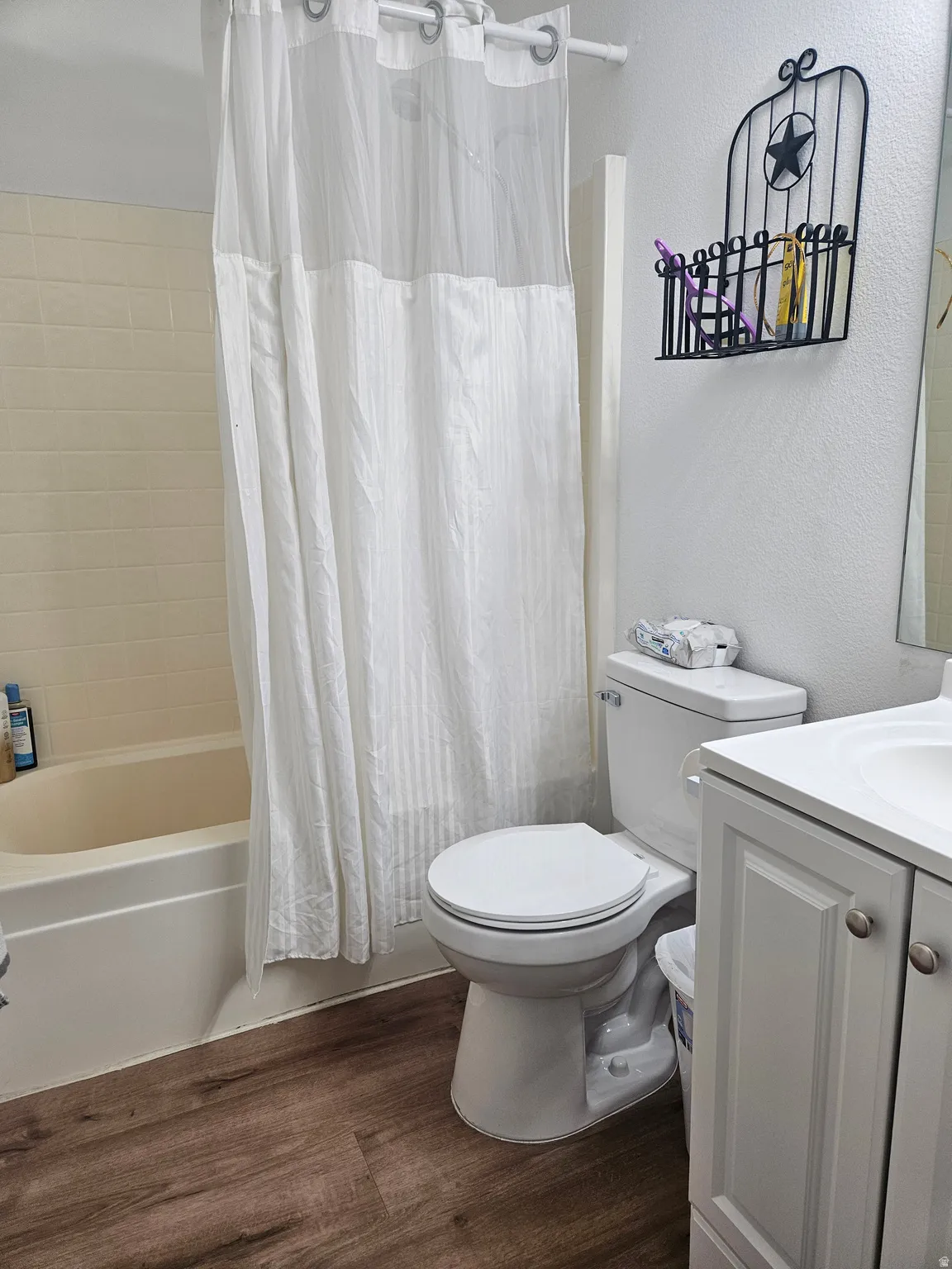 Bathroom featuring a white toilet, single-sink vanity with white cabinetry, a bathtub with a shower, and wood-finish flooring