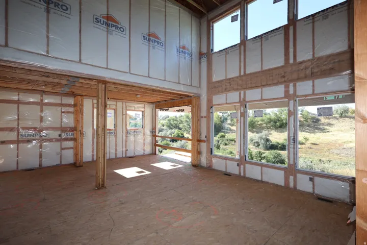 Expansive interior space featuring structural wood framing, a two-story window arrangement, and plywood subflooring