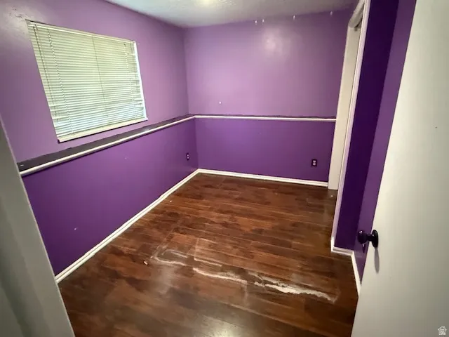 Room with wood-finish flooring, a window featuring horizontal blinds, and a white trim baseboard