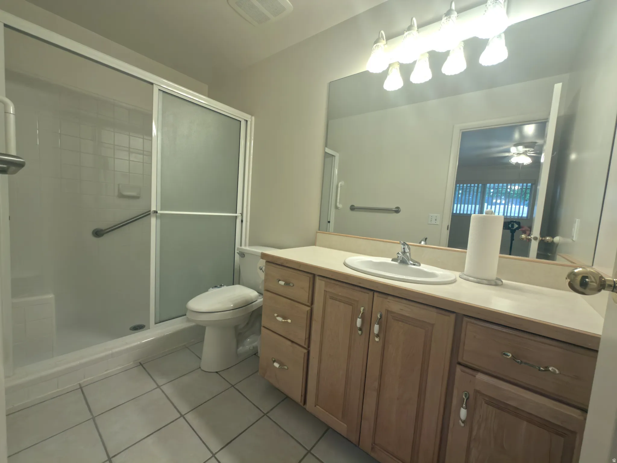 Bathroom featuring a wood-finish vanity with an integrated sink, a large wall-mounted mirror, and a shower with sliding frosted glass doors