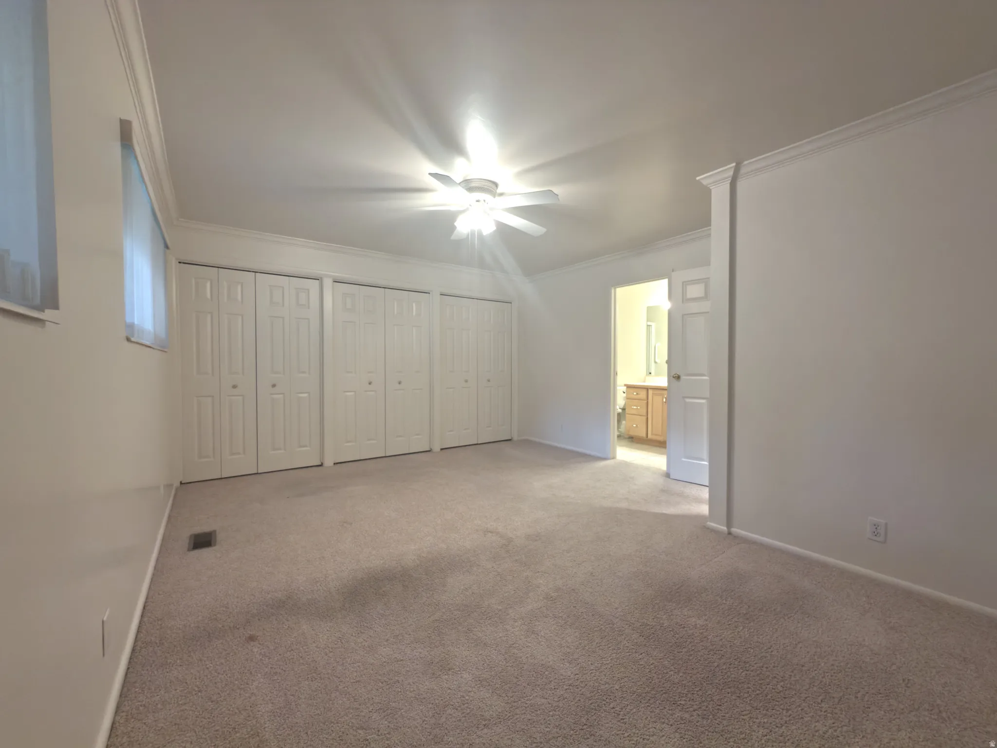 Spacious room featuring multiple bi-fold closet doors, wall-to-wall carpeting, and a ceiling fan with light fixture