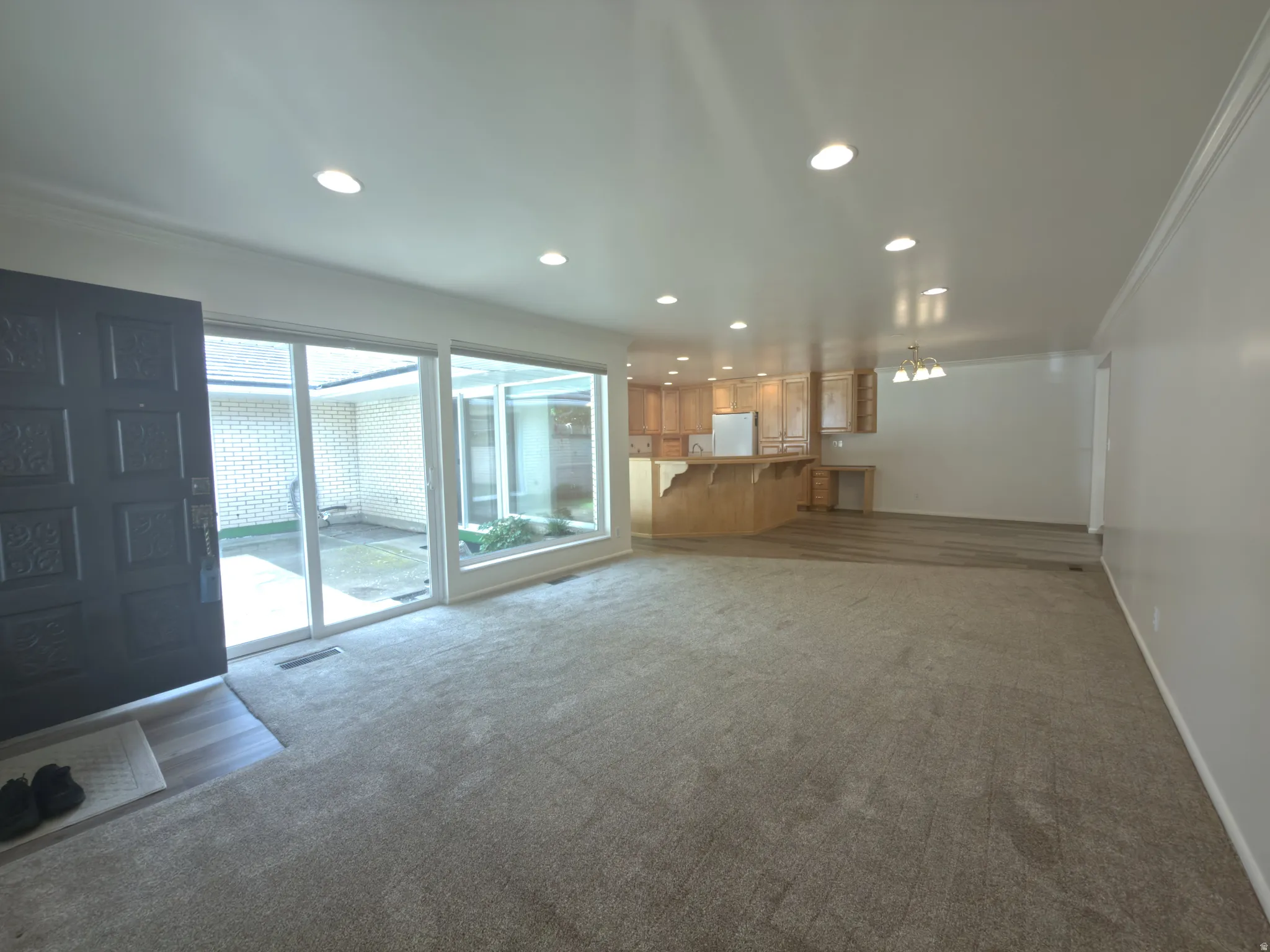 Open-concept living area featuring a dark paneled entry door, light gray carpet, recessed lighting, and expansive windows