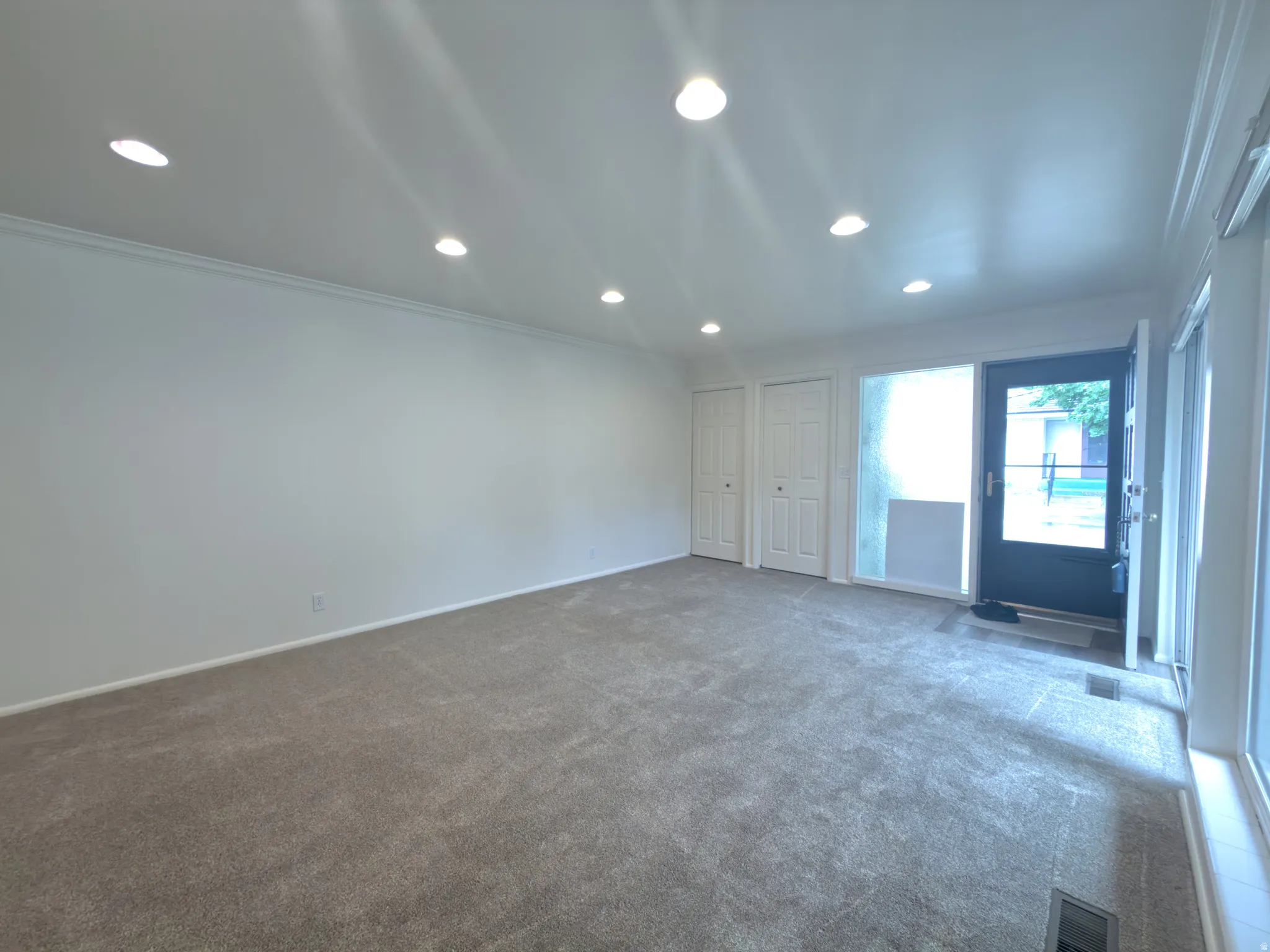 Spacious room featuring neutral carpeting, recessed ceiling lighting, crisp white walls, and crown molding