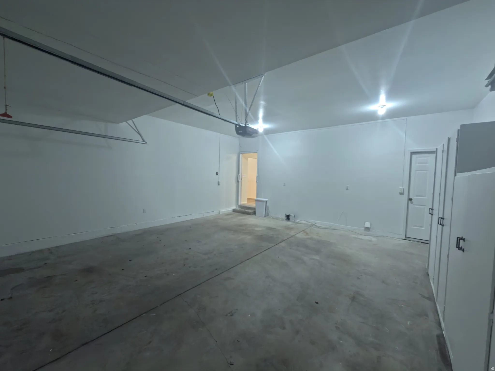 Spacious garage featuring a concrete floor, bright overhead lighting, white painted walls, and built-in storage cabinets