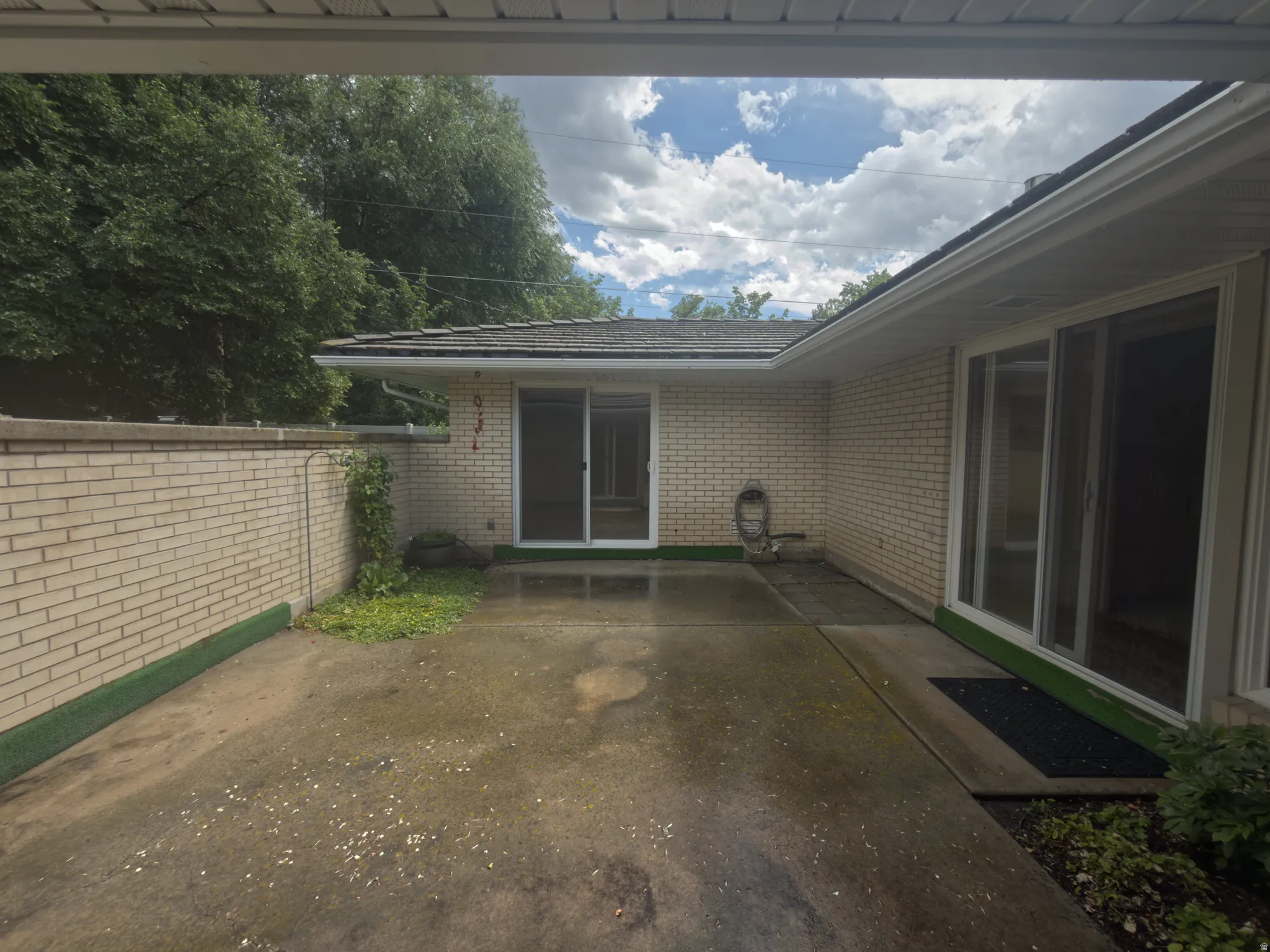 Exterior patio area featuring concrete paving, a light-colored brick privacy wall, and brick exterior siding