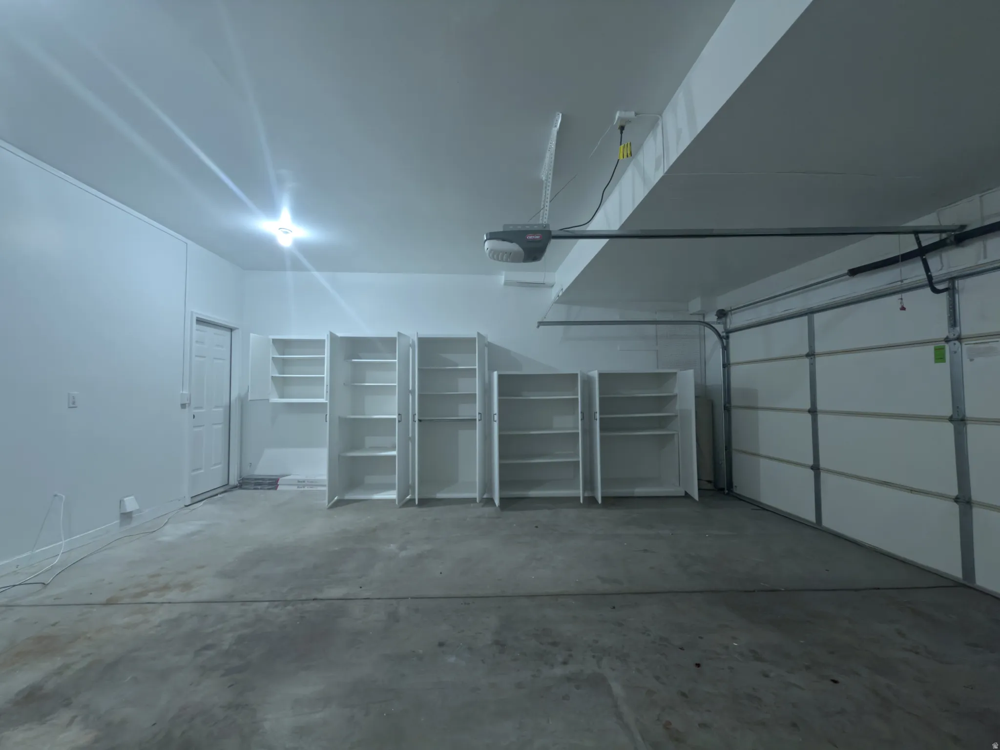 Spacious garage with concrete flooring, multiple built-in shelving units, a painted overhead garage door, and a single interior access door