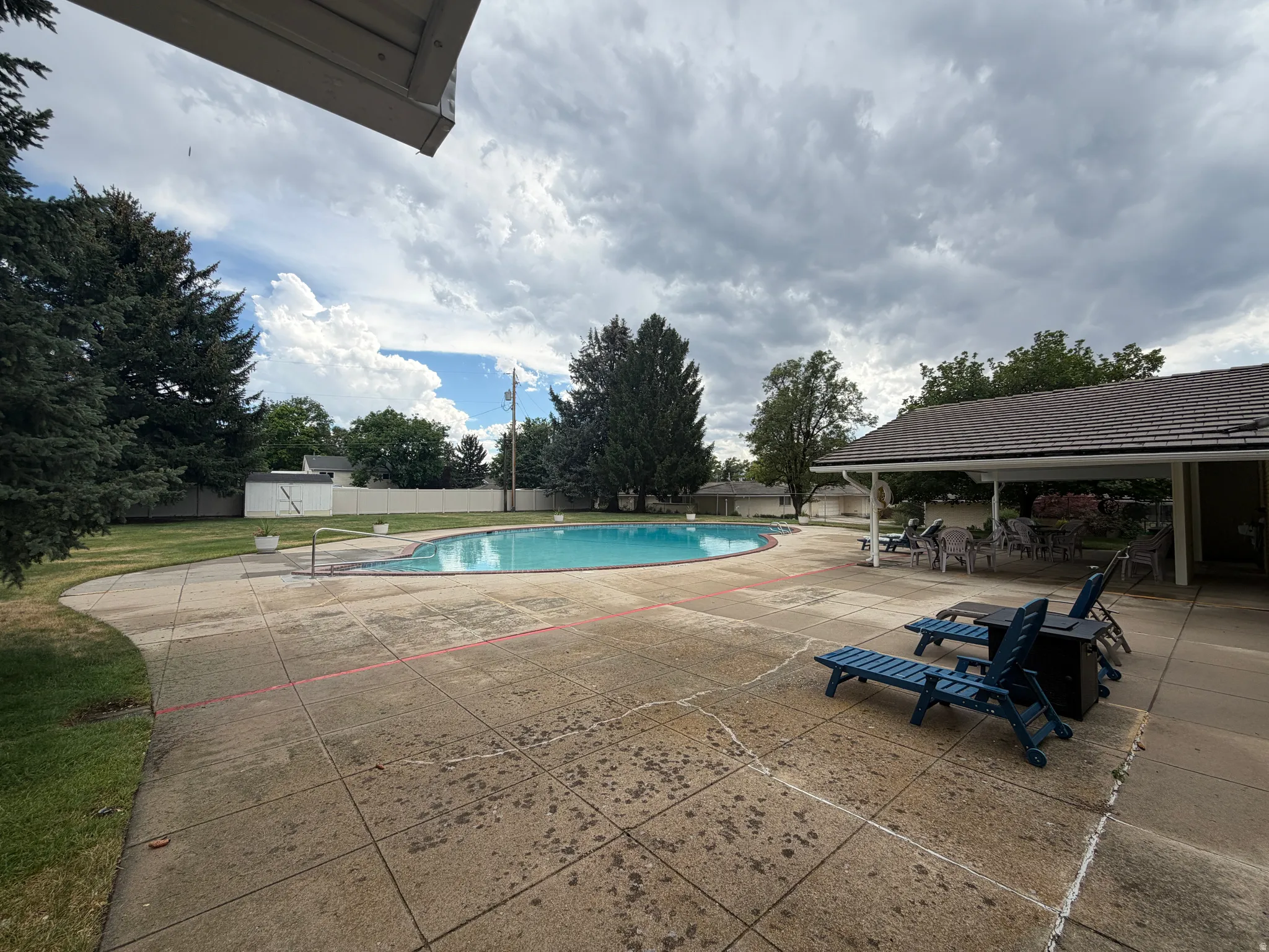 Club House Expansive outdoor area featuring a kidney-shaped swimming pool, a large concrete patio, and mature perimeter trees