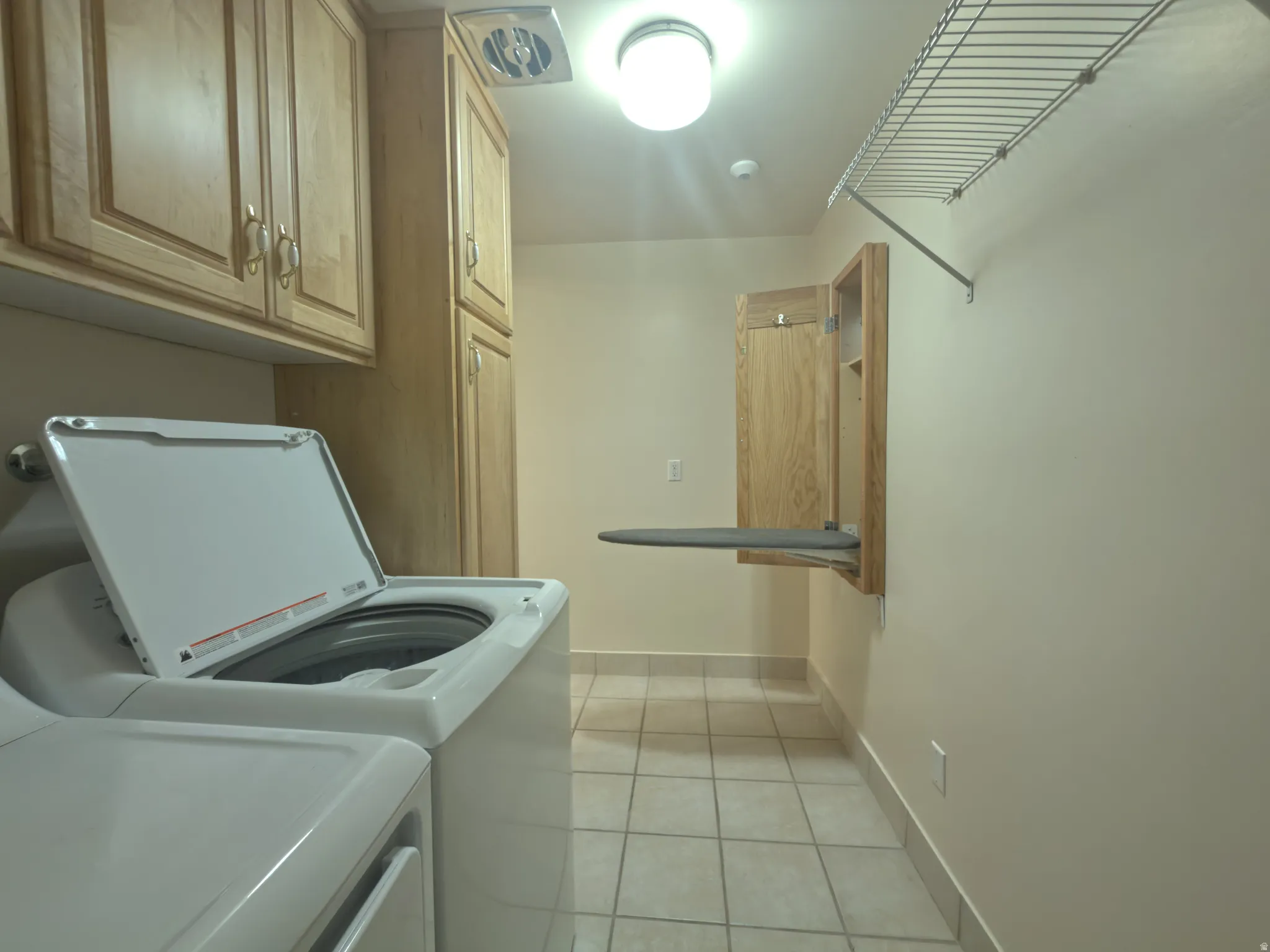 Laundry room featuring extensive wood-finish cabinetry, a built-in folding ironing board, a wall-mounted wire shelf, tile flooring, and overhead lighting