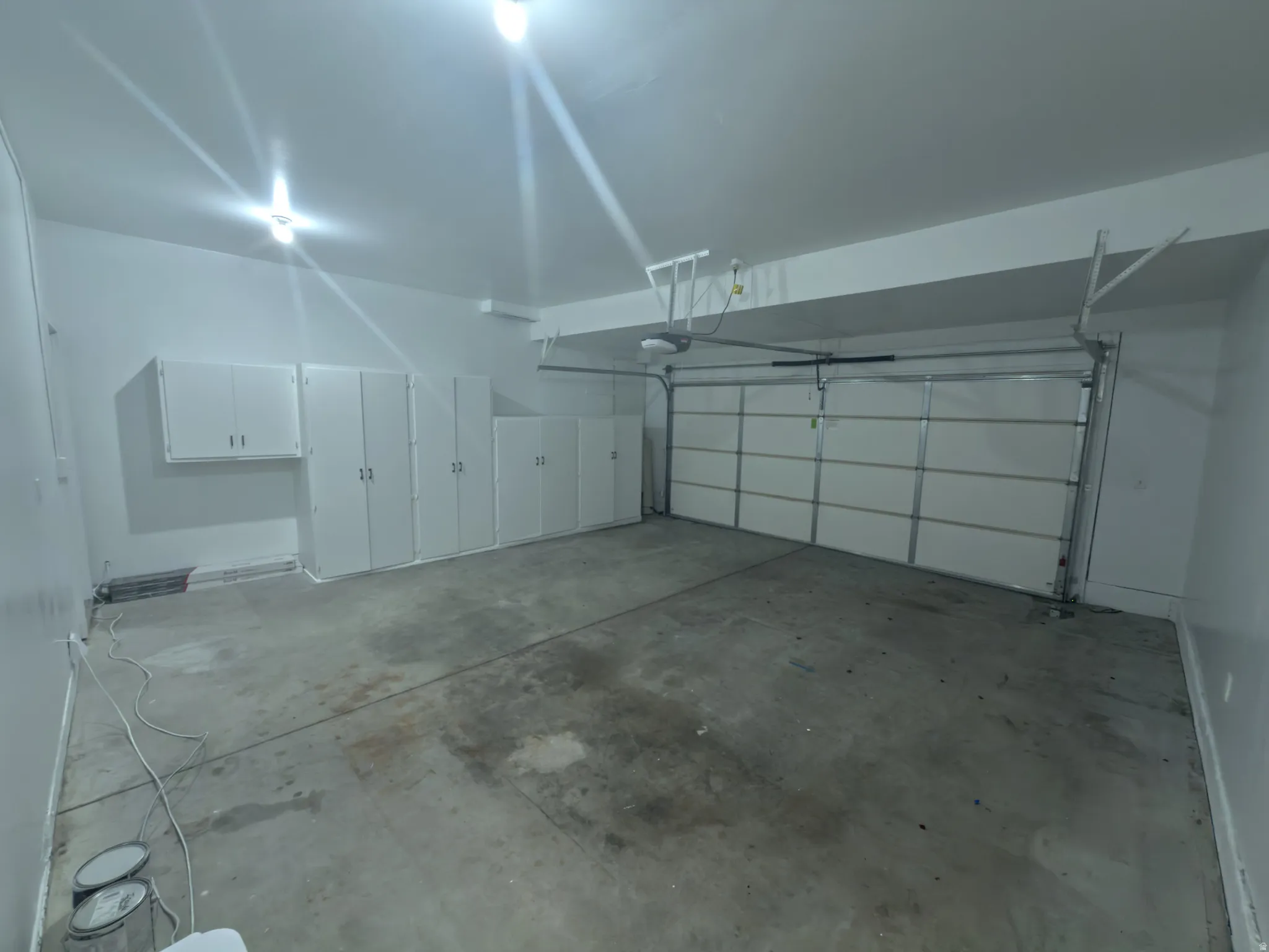 Spacious garage featuring extensive built-in white cabinetry, concrete flooring, and an overhead garage door with an automatic opener