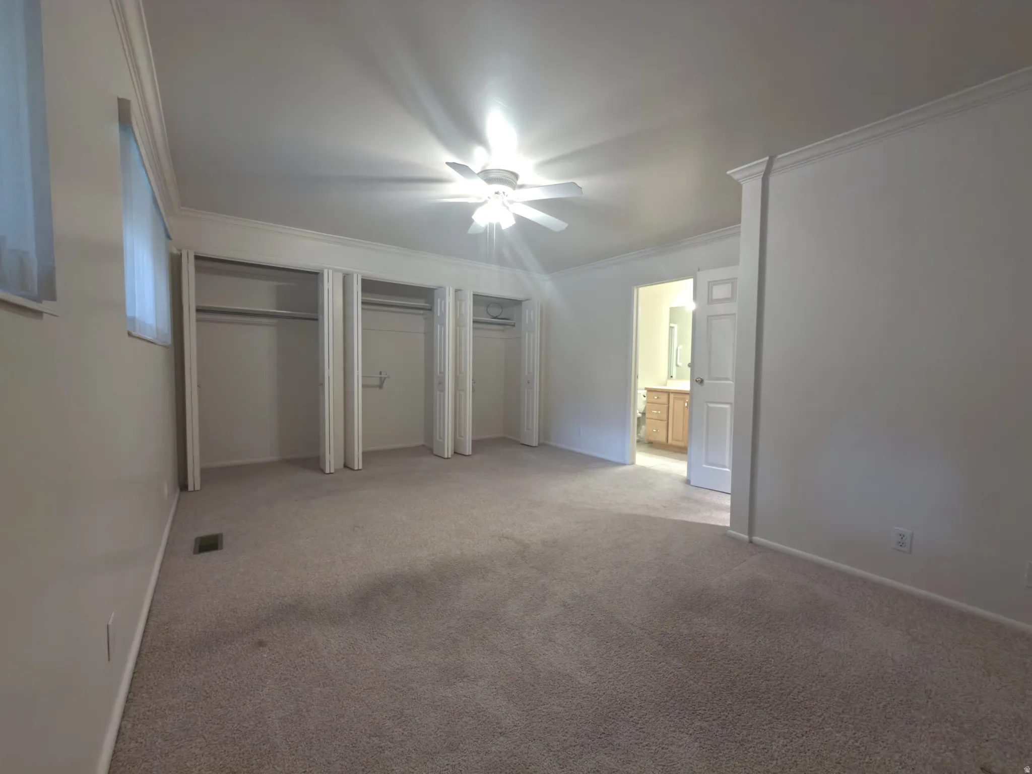 Carpeted interior space featuring multiple open closets with hanging rods, a ceiling fan with integrated lighting, and a doorway revealing a bathroom vanity with a wood-finish cabinet