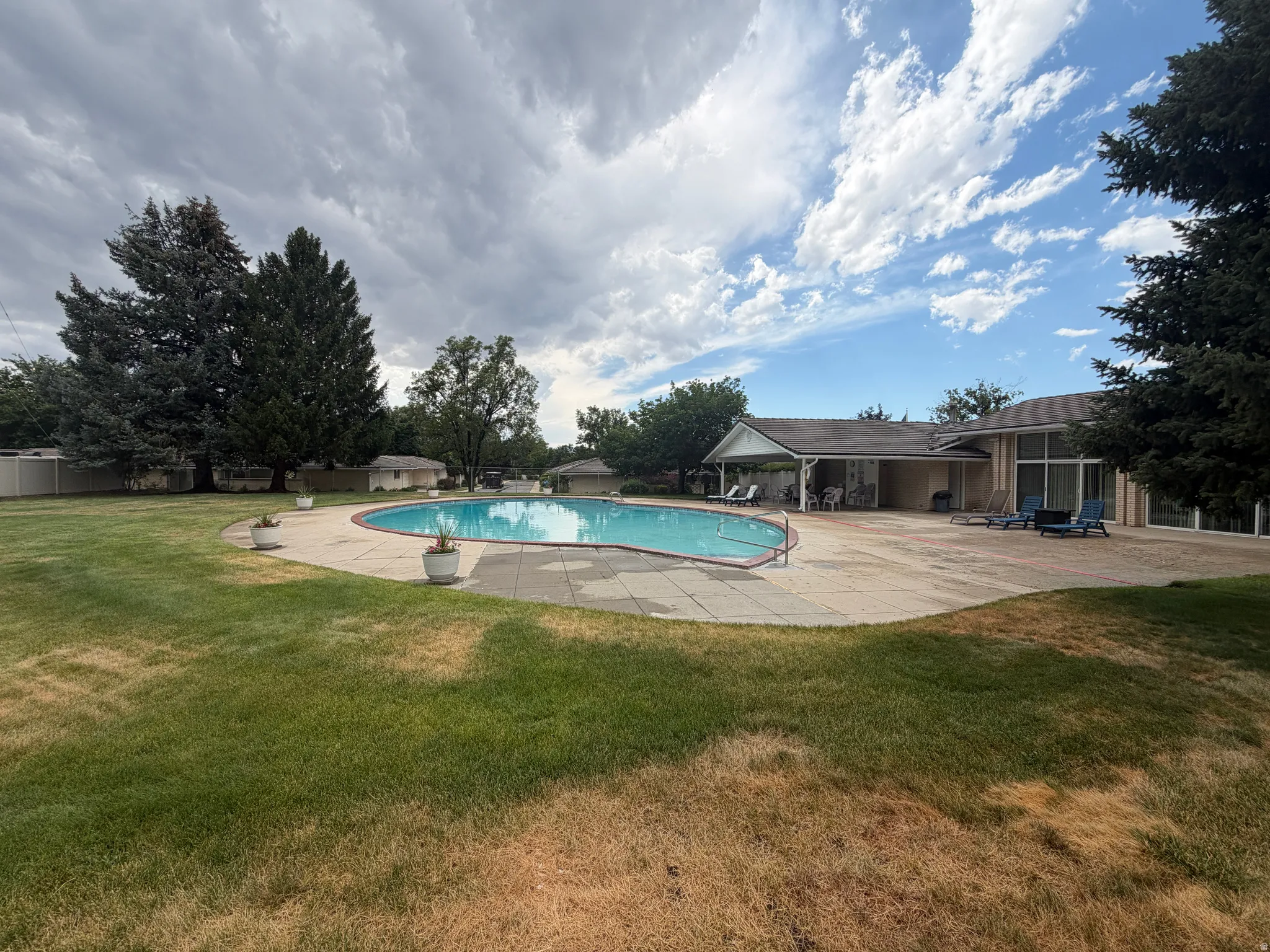 Club House Expansive backyard featuring a large swimming pool with concrete surround, mature trees, and a covered patio area