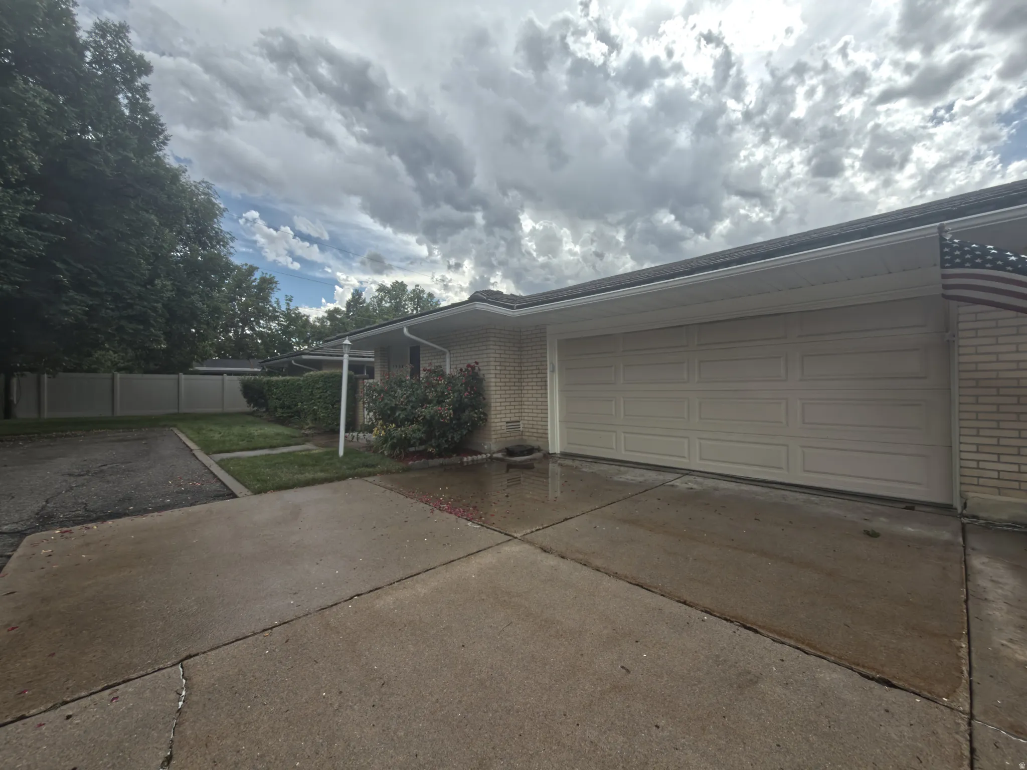 Brick exterior featuring a two-car garage with a panel door, concrete driveway, and established front landscaping