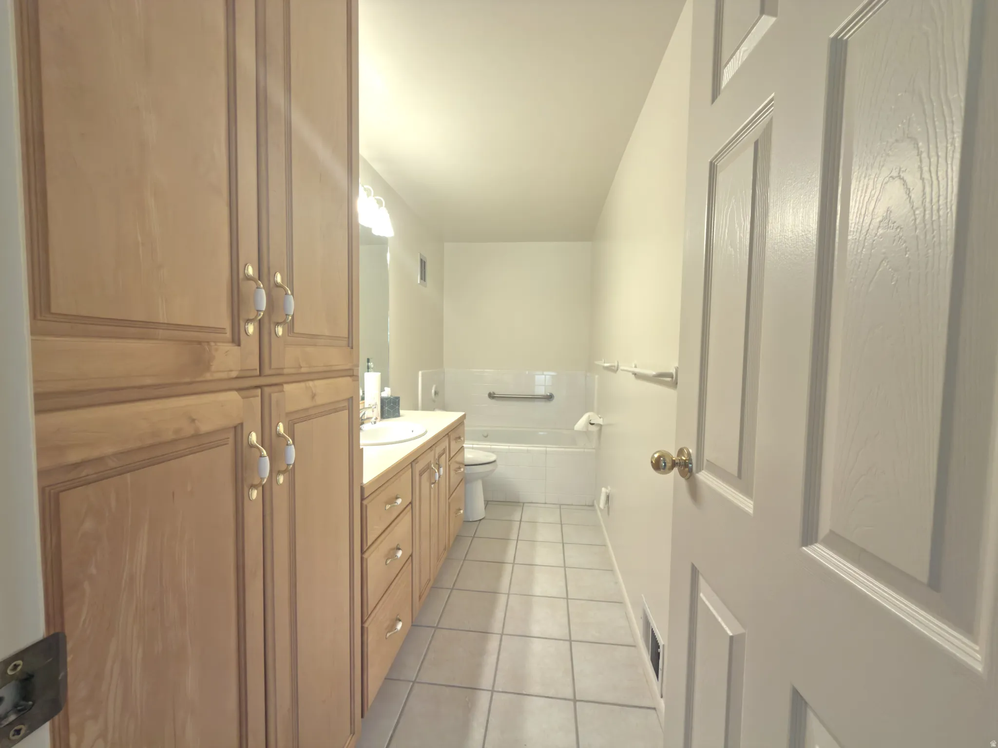 Bathroom featuring extensive wood cabinetry, a built-in vanity with a single sink, a large soaking tub, and tile flooring