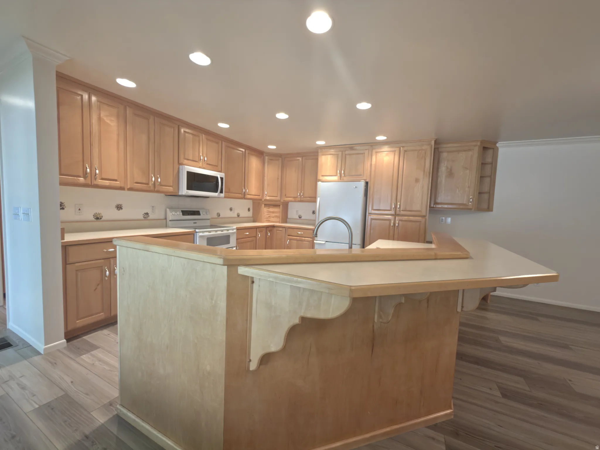 Kitchen featuring light wood cabinetry, recessed lighting, stainless steel appliances, and a central island with a breakfast bar