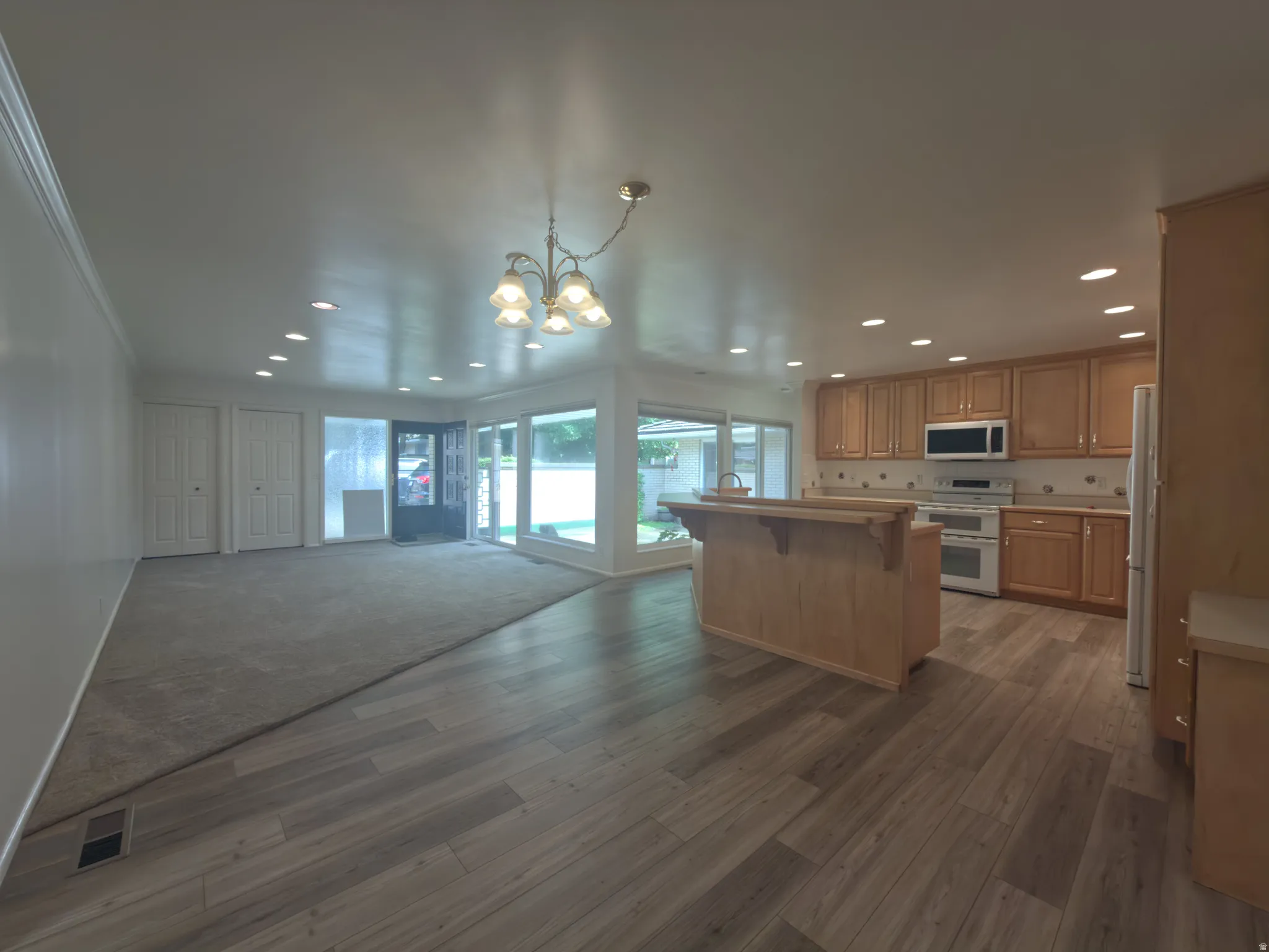 Open-concept living area featuring wood-finish flooring, a kitchen with natural wood cabinetry, and a central island with a breakfast bar
