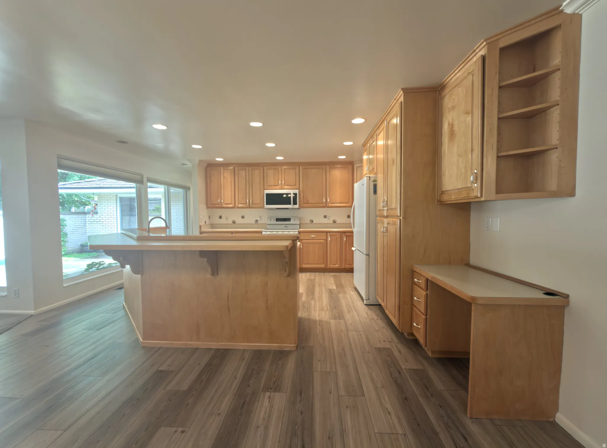 Open-concept kitchen featuring extensive light wood cabinetry, recessed lighting, and wood-finish flooring