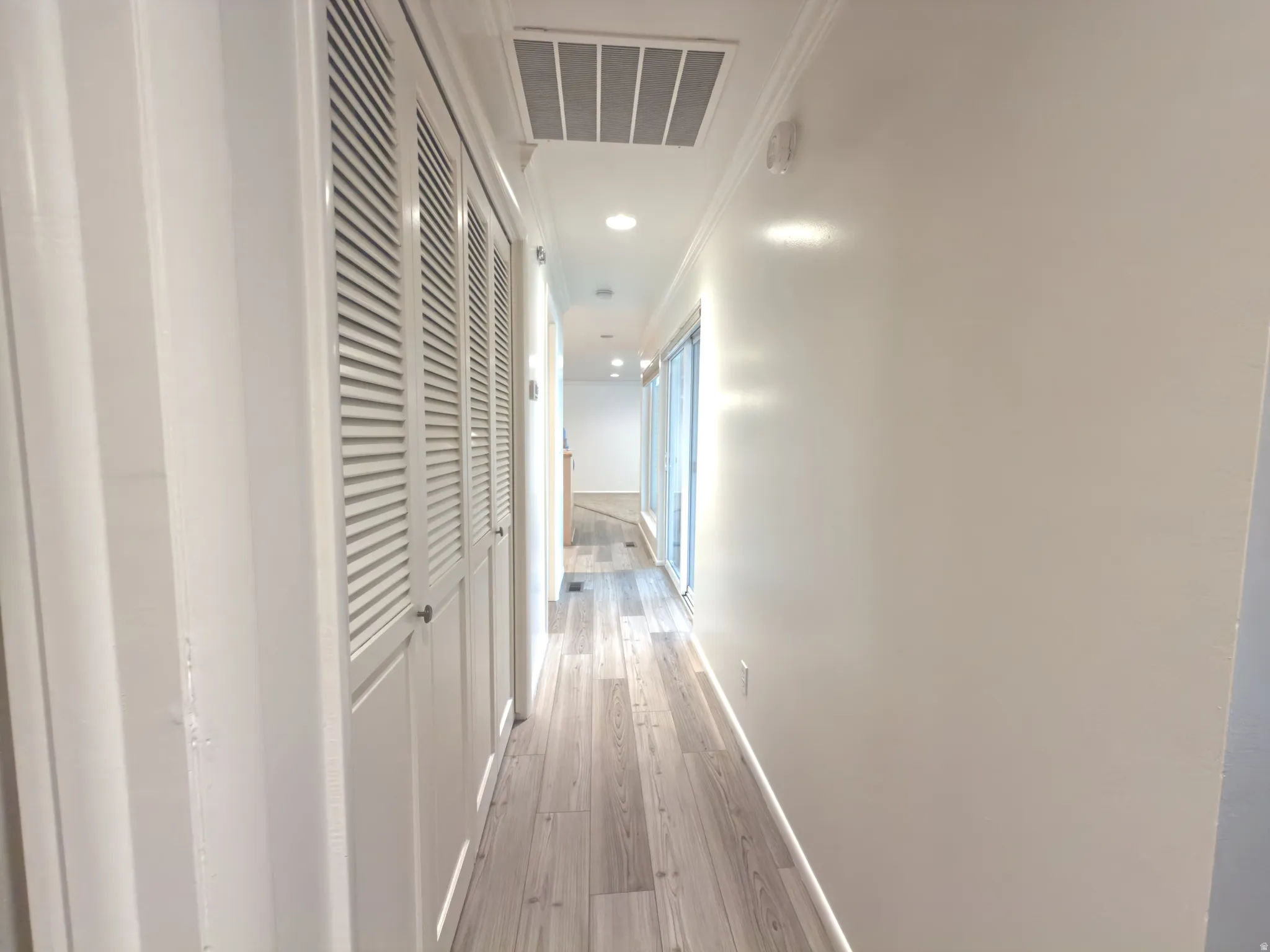 Long hallway featuring wood-finish flooring, recessed lighting, white louvered closet doors, and crown molding