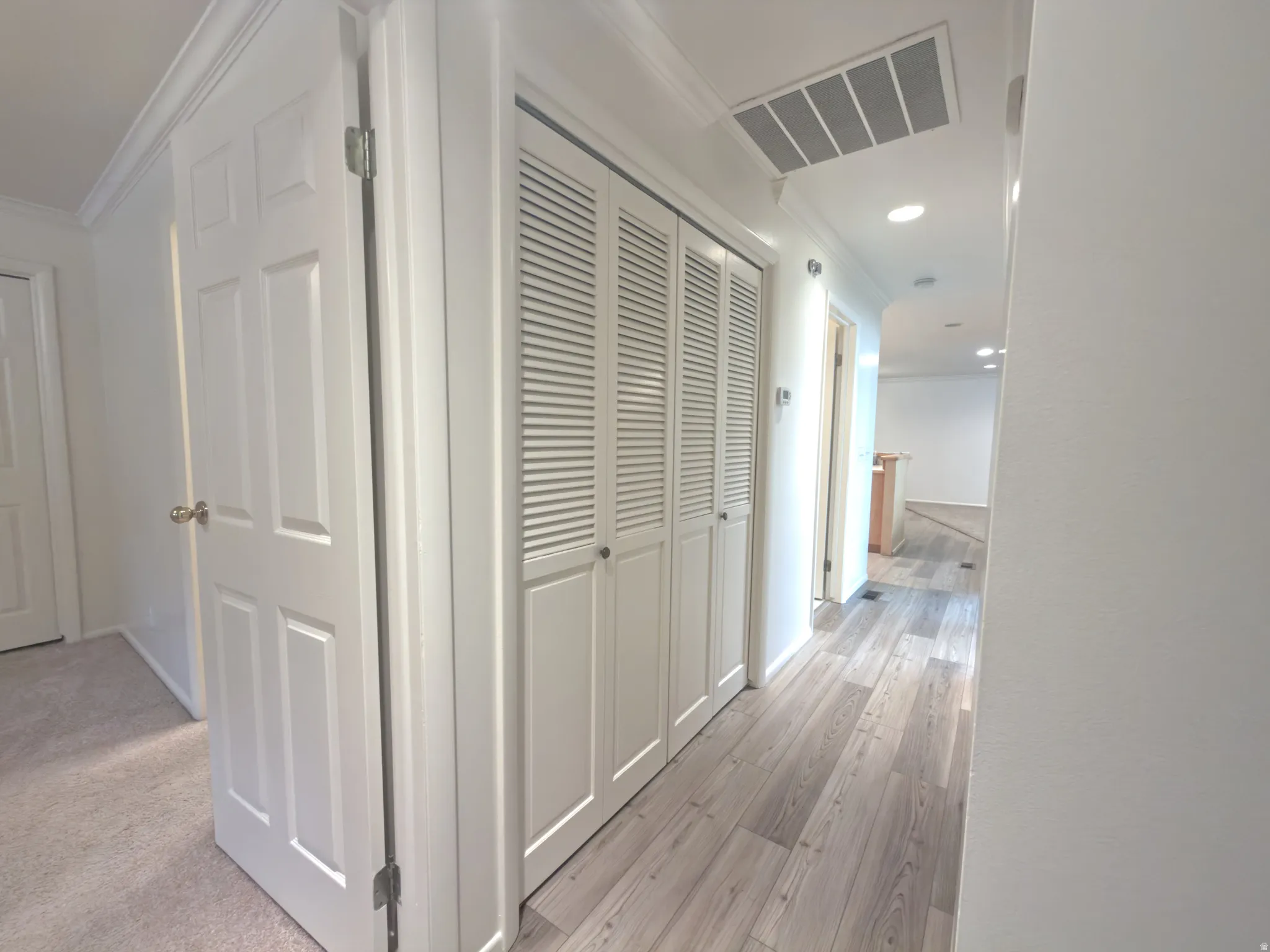 Hallway featuring light wood-finish flooring, white paneled doors, louvered closet doors, recessed lighting, and crown molding