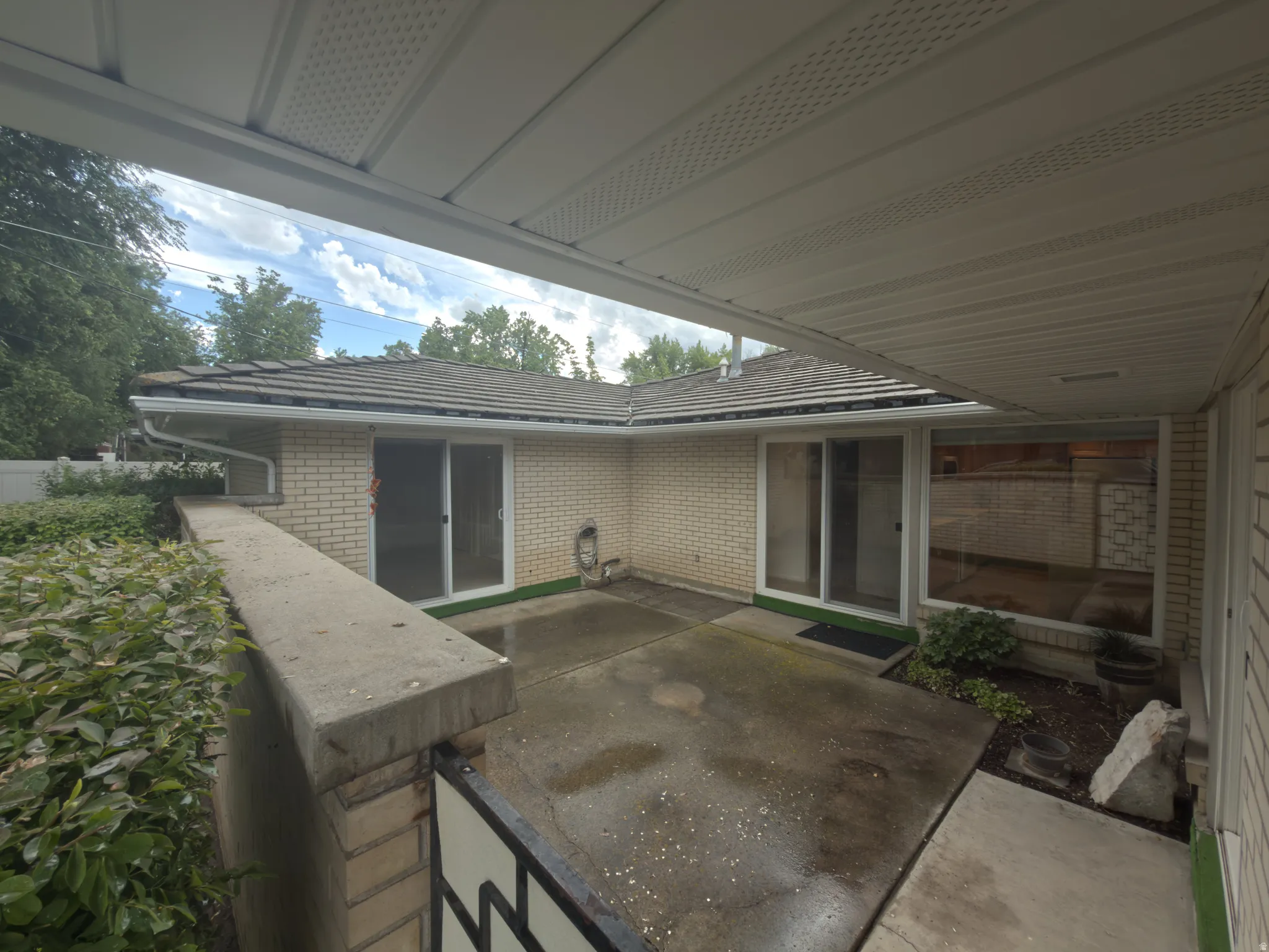 Covered patio space featuring concrete flooring, a brick half-wall, and mature landscaping