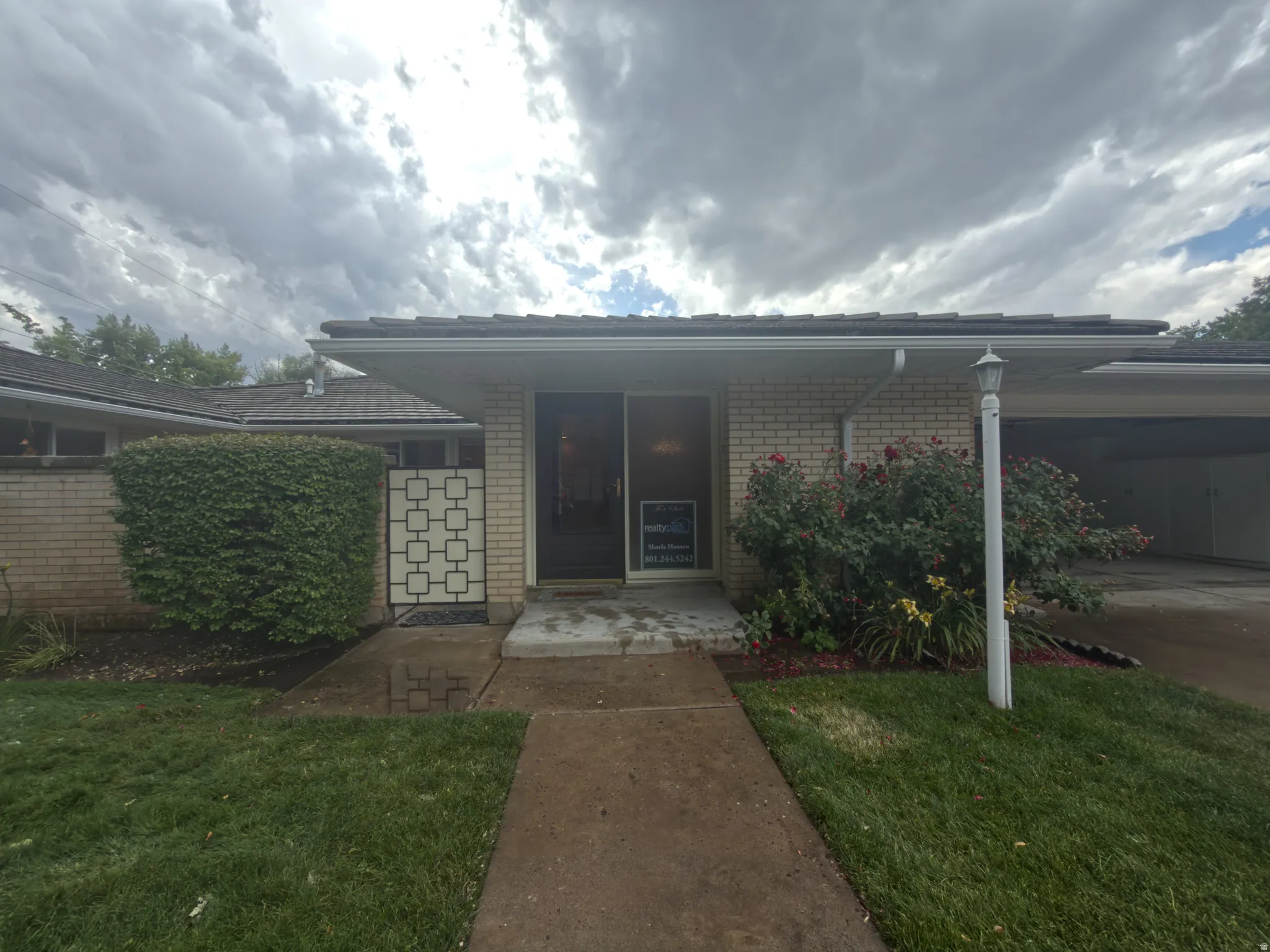 Front exterior featuring light-colored brick, a covered entry, and a carport