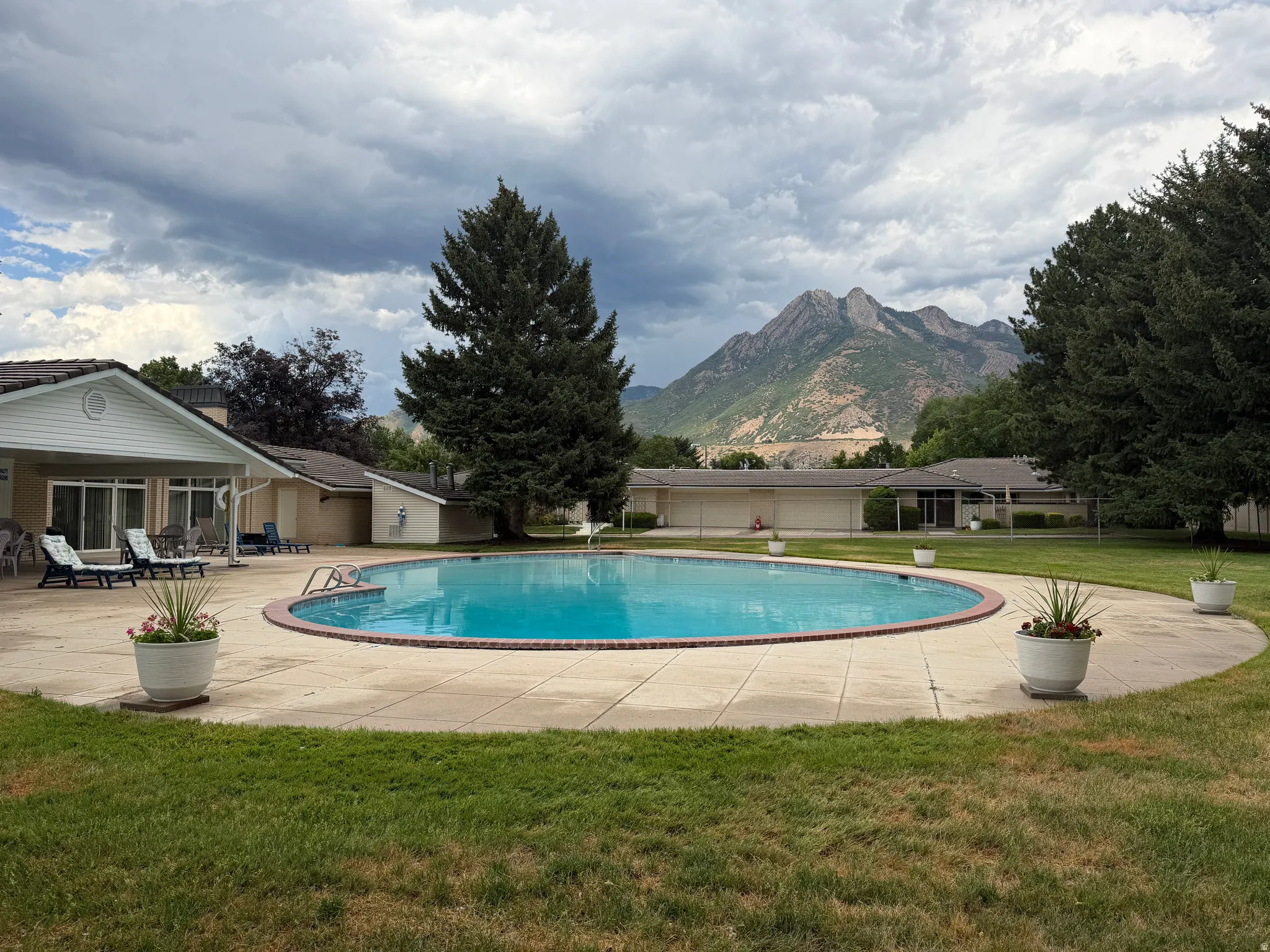 Club House swimming pool with concrete surround, expansive green lawn, mature trees, and mountain scenery