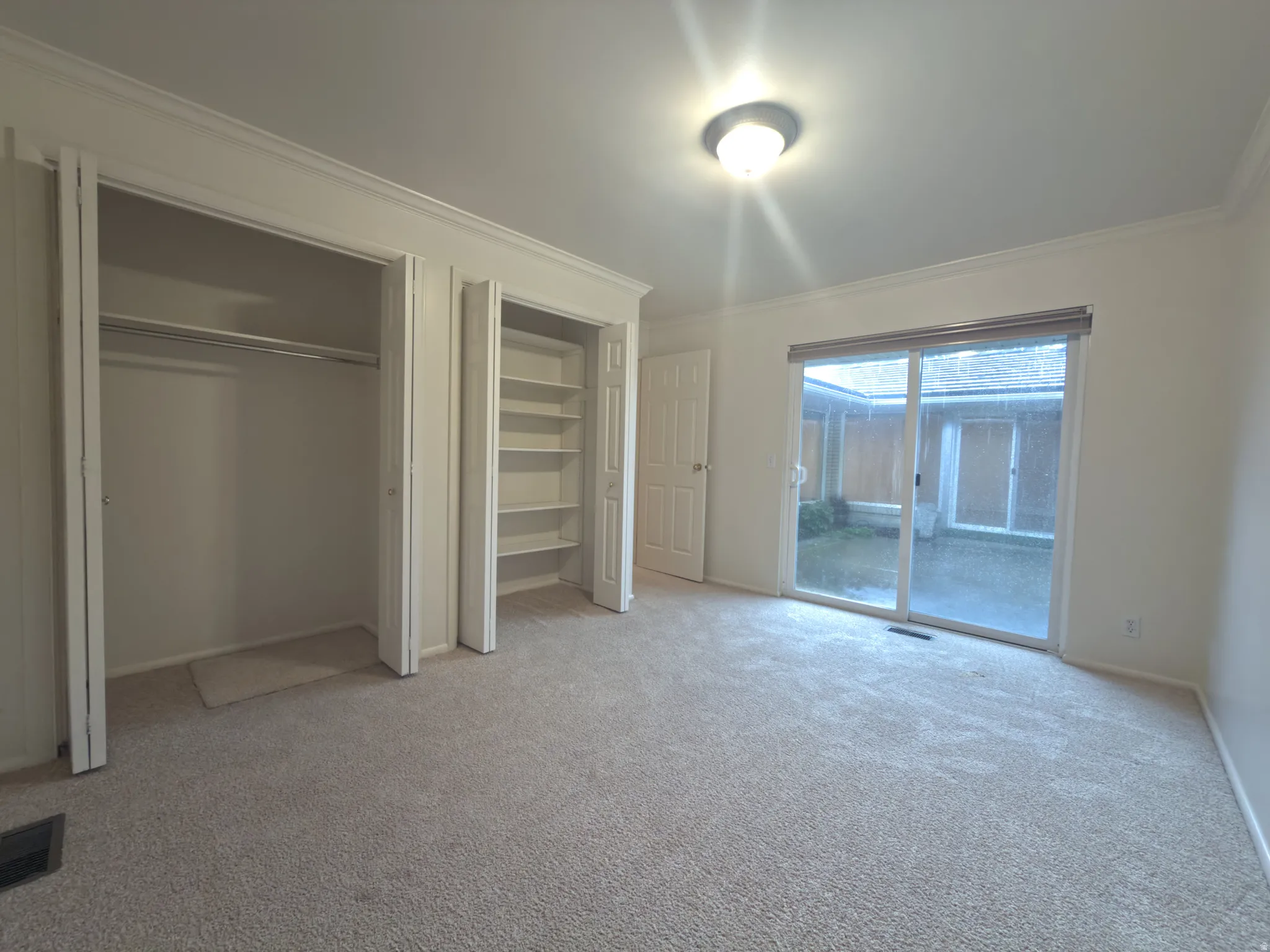 Spacious room featuring light-toned carpet, crown molding, and a ceiling-mounted light fixture